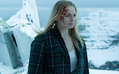 Em uma montanha coberta de neve, Sophie Turner aparece com um corte na cabeça, e sangue no rosto, na série Survive