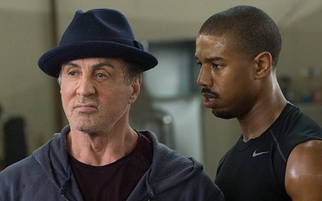 Sylvester Stallone olha para frente enquanto Michael B. Jordan o encara pelo lado direito em cena de Creed - Nascido Para Lutar