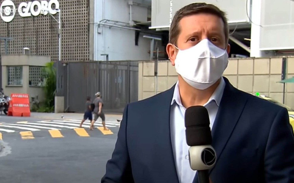De máscara branca, o repórter Sylvestre Serrando faz reportagem na frente da sede da Globo no Rio de Janeiro