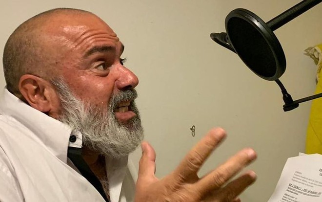 O ator André Mattos gesticula diante de um microfone, com o roteiro da série #tdvaificar... na mão