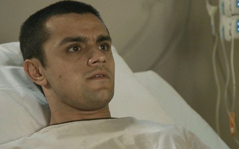 O ator Felipe Simas está deitado em uma cama de hospital com expressão de medo em cena de Salve-se Quem Puder