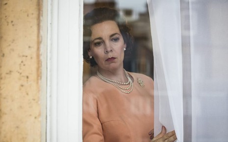 Olivia Colman olha pela janela em cena de The Crown