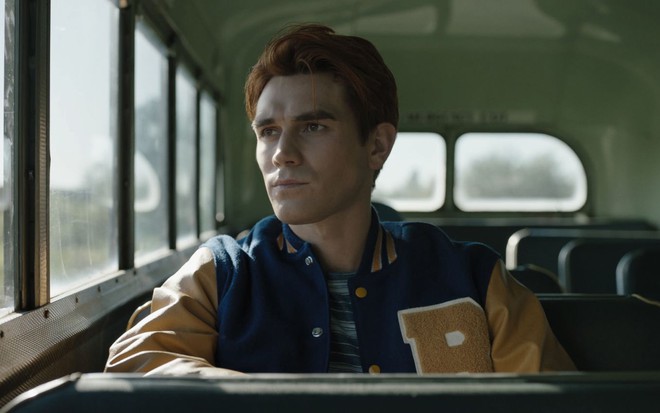Com jaqueta de jogador de futebol americano, KJ Apa olha pela janela do ônibus em cena de Riverdale