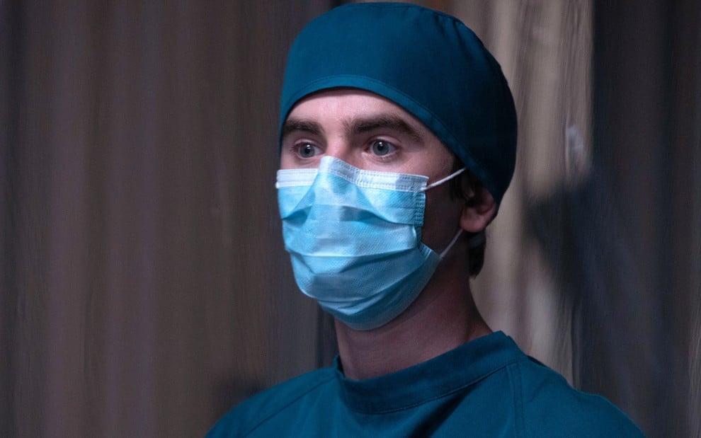 Freddie Highmore com uma máscara cirúrgica azul, e usando um protetor na cabeça, em cena de Good Doctor