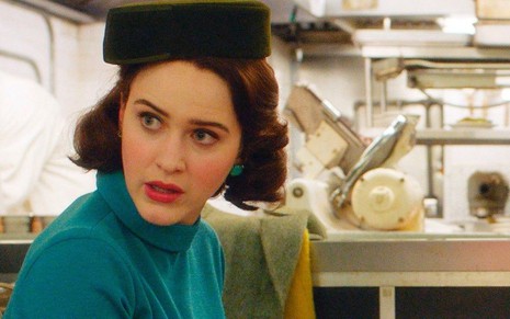 Em um restaurante e com um vestido verde de dondoca, Rachel Brosnahan faz cara de atônita em The Marvelous Mrs. Maisel