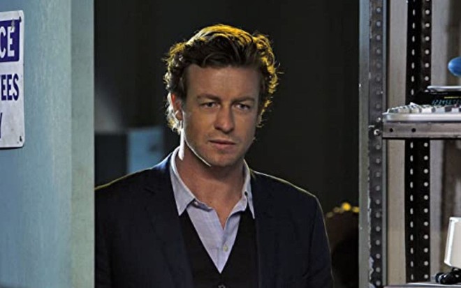 O personagem Patrick Jane (Simon Baker) entra pela porta de uma sala na série The Mentalist