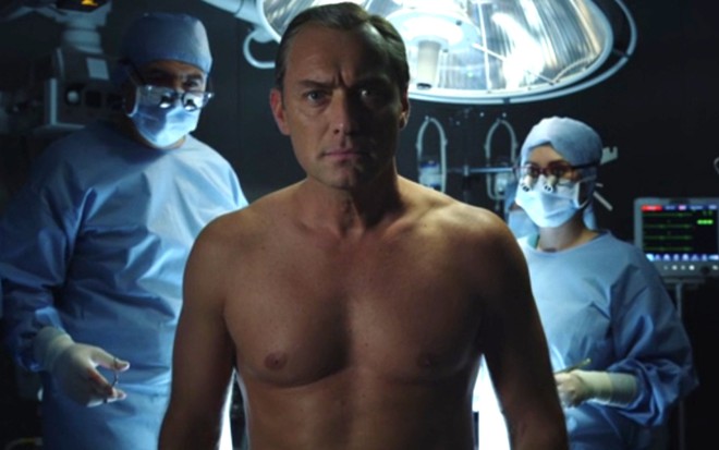 Sem camisa, Jude Law está em uma sala de cirurgia no primeiro episódio da série The New Pope