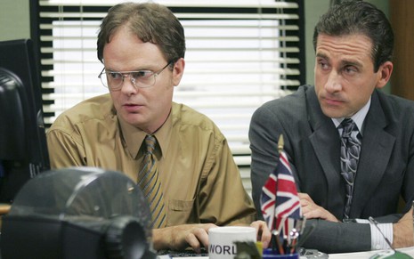 Observado por Steve Carell, um concentrado Rainn Wilson mexe em um computador em cena da série The Office
