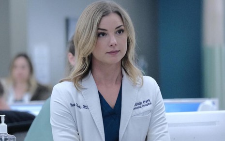 Com um jaleco branco de médica, a loira Emily VanCamp cruza os braços em cena da terceira temporada de The Resident