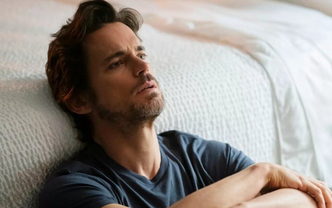 Sentado no chão, o ator Matt Bomer encosta a nuca em uma cama e olha para o teto em cena da série The Sinner