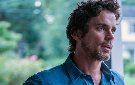 Na varanda de uma casa em um bairro rico, Matt Bomer aparece de camisa azul em cena da terceira temporada de The Sinner