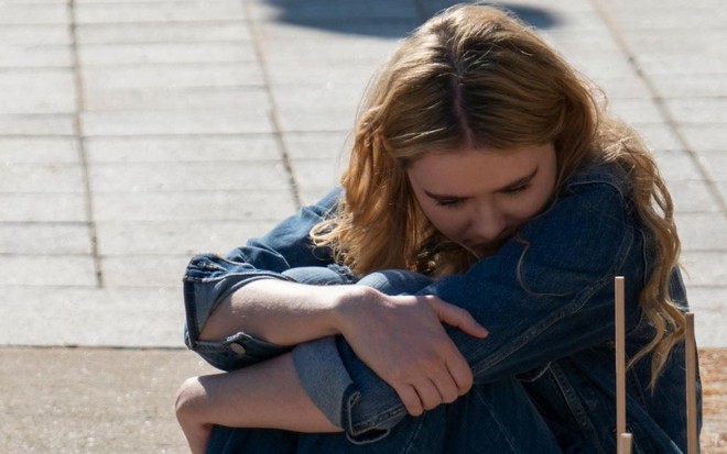 Sentada no chão, Kathryn Newton abraça os joelhos e cobre o rosto com um dos braços em cena da série The Society