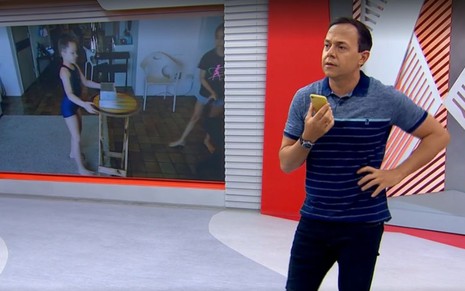 Tiago Medeiros, apresentador do Globo Esporte, com a mão na cintura e o celular na outra mão