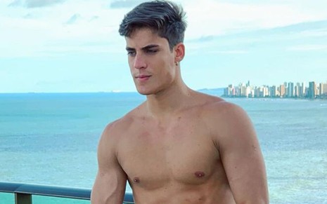 Imagem de Tiago Ramos sem camisa, em uma cobertura em frente ao mar