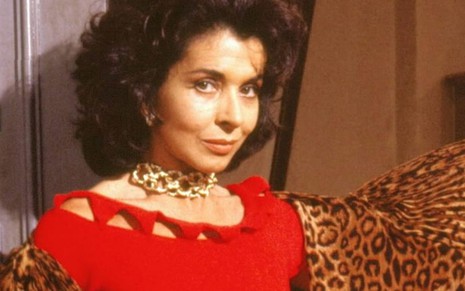 A atriz Betty Faria caracterizada como Tieta, olhando para câmera, de vestido vermelho e colar dourado