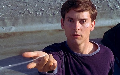 O ator Tobey Maguire com expressão de curiosidade ao lançar uma "teia de aranha" pela mão no filme Homem-Aranha