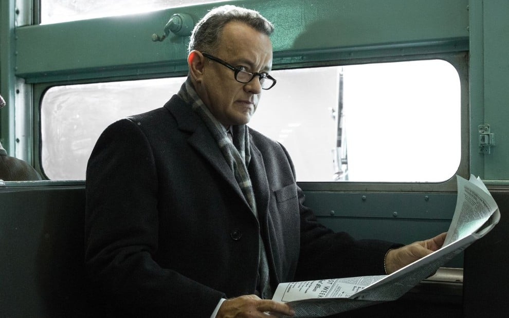 Em um trem, Tom Hanks lê jornal em cena do filme Ponte dos Espiões (2015)