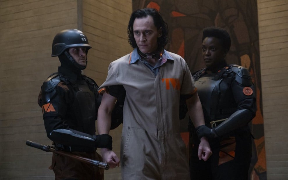 Tom Hiddleston (ao centro) sendo segurado por dois guardas em cena de Loki