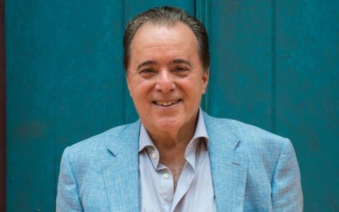 Tony Ramos sorridente, em sessão de fotos usando terno azul claro e camisa combinando