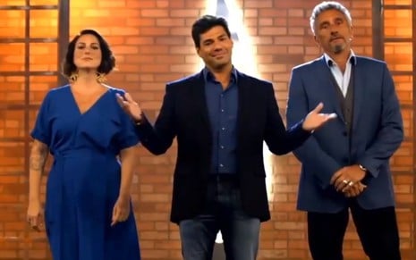 Ailin Aleixo, Felipe Bronze e Emmanuel Bassoleil lado a lado dentro de um cenário de reality show