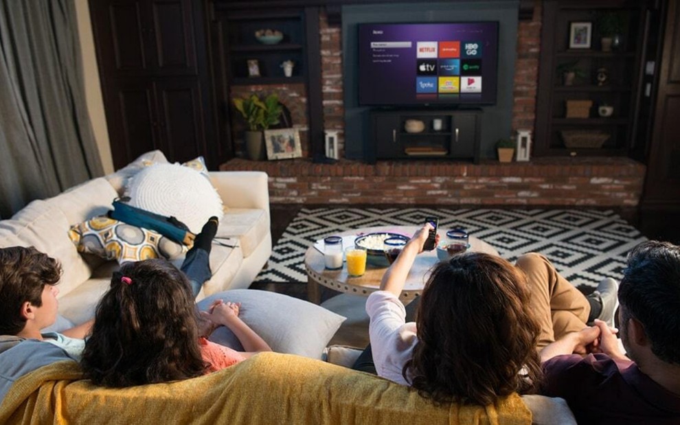 Família no sofá escolhe o serviço de streaming que quer assistir na tela da TV
