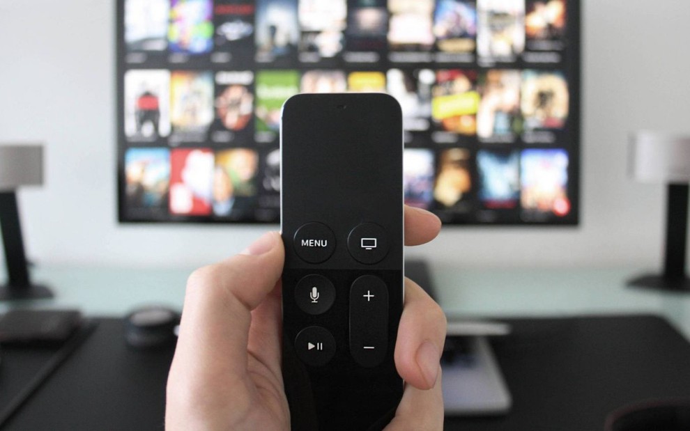 Mão segura controle remoto diante de uma smart TV ligada na Netflix