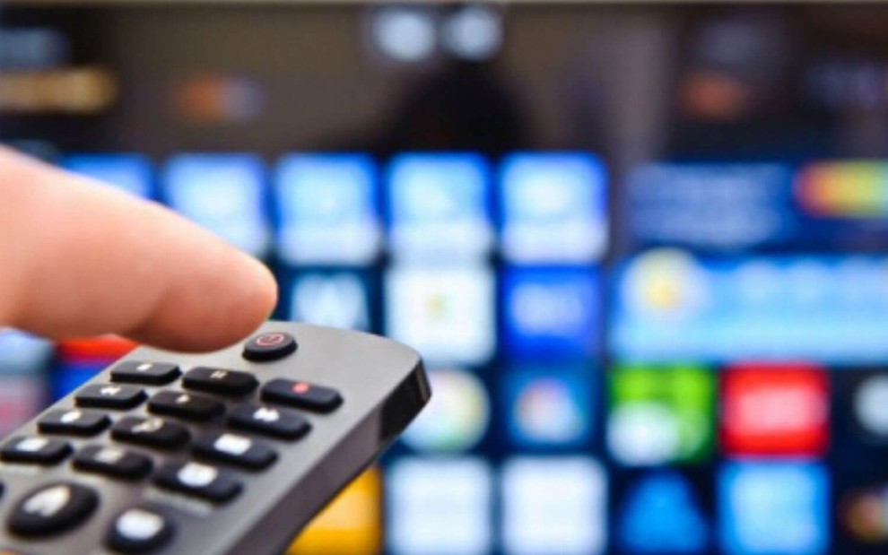 Imagem de uma pessoa usando o controle remoto na frente de uma televisão