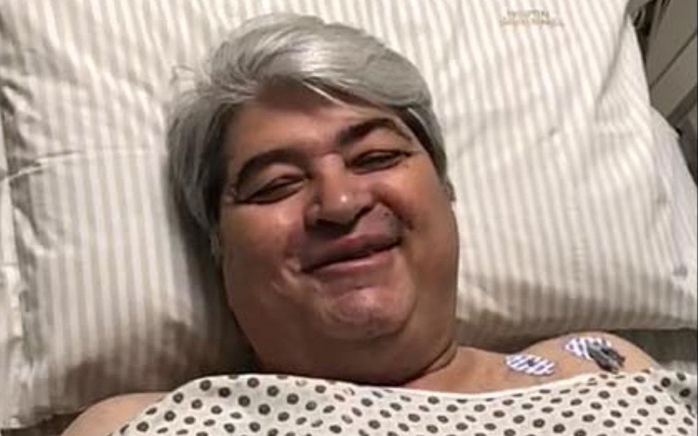 O apresentador José Luiz Datena sorrindo em vídeo publicado nas redes sociais na noite de domingo (25) em que aparece deitado em uma cama de hospital e vestindo uma camisola hospitalar