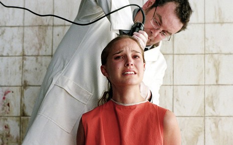Natalie Portman como Evey sentada em uma cadeira com um homem raspando a sua cabeça em cena de V de Vingança