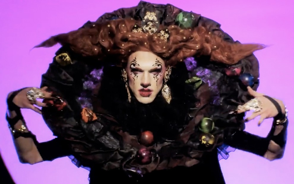 A drag queen Utica com uma maquiagem escura, vampiresca, com cabelos ruivos em forma de chifre, e uma grande quantidade de tecido em forma circular ao redor da cabeça durante mini-challenge de Rupaul's Drag Race
