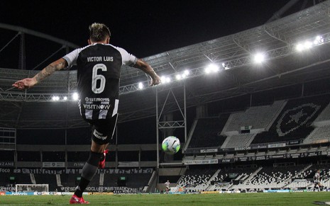 O jogador do Botafogo Victor Luis de costas em lance com bola no ar vestido com uniforme do time nas cores preto e branco