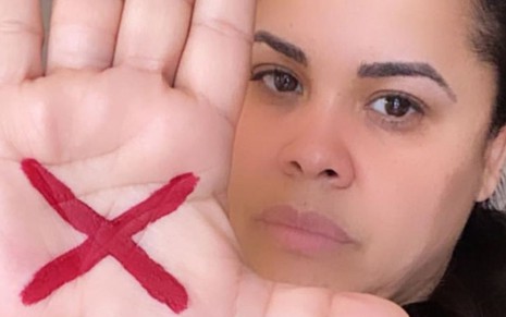 Selfie da cantora Cassiane mostrando um X na cor vermelha riscado na palma de sua mão