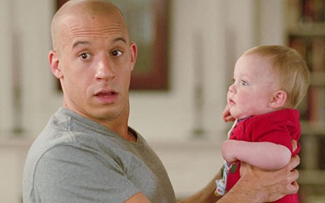 Vin Diesel com expressão de desespero enquanto segura um bebê em cena de Operação Babá (2005)