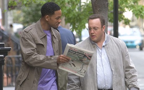 Caminhando na rua, Will Smith mostra um jornal para Kevin James em cena de Hitch - Conselheiro Amoroso (2005)
