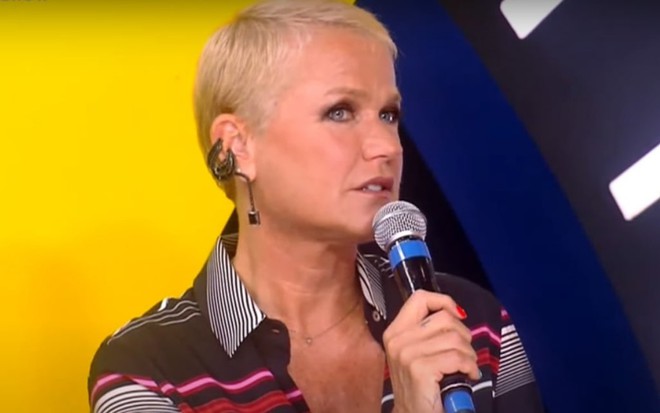 Xuxa Meneghel, com microfone na mão e cabelos bem curtinhos, fala durante o Domingo Show de 8 de março