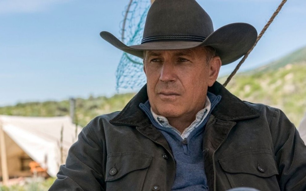 Sentado em uma cadeira, Kevin Costner aparece com chapéu de caubói e olha para o infinito em cena de Yellowstone