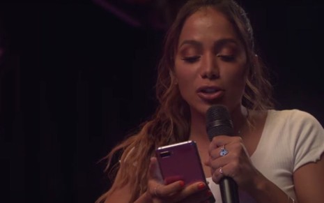 A cantora Anitta em live no YouTube em 10 de maio segurando um celular e falando em um microfone
