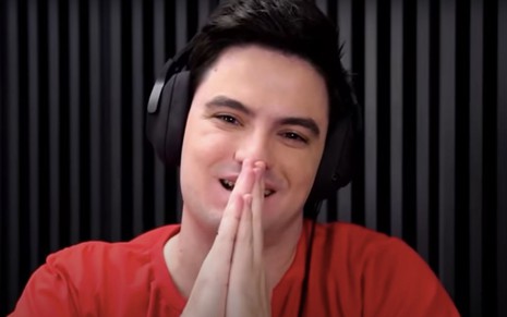 O youtuber Felipe Neto em seu vídeo mais recente publicado no YouTube; ele aparece com fazendo sinal de prece com as mãos e veste camiseta vermelha e fones de ouvido