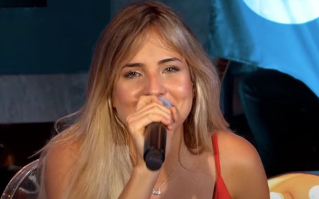 A cantora Gabi Martins sentada e com o microfone na mão