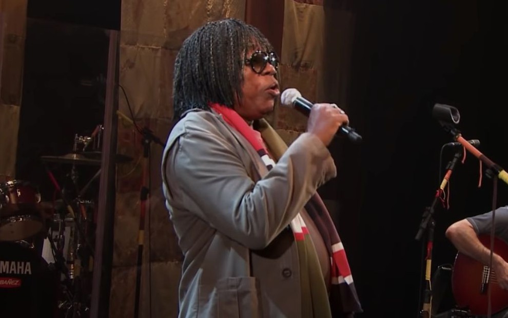 Milton Nascimento canta no clipe da música Travessia: músico usa casaco e óculos escuros