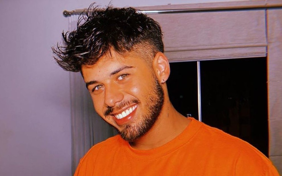 Imagem de Zé Felipe sorrindo com camisa laranja em ensaio fotográfico