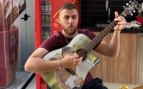 Zé Neto tocando violão com uma geladeira vermelha ao fundo