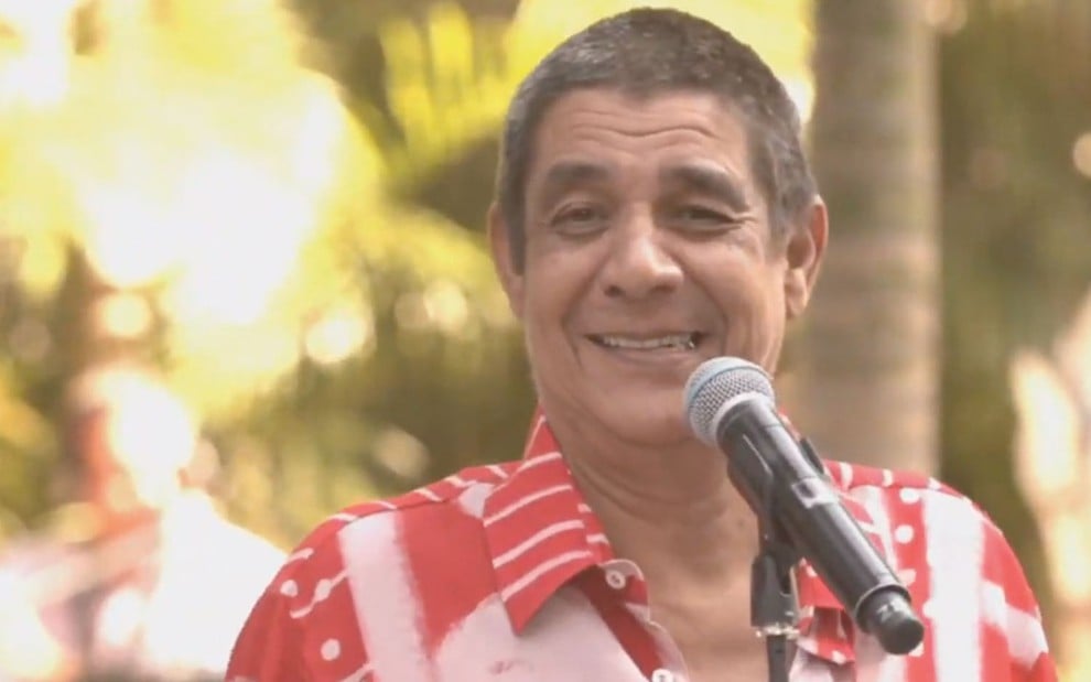 Zeca Pagodinho com uma blusa listrada vermelha e branco em frente a um microfone