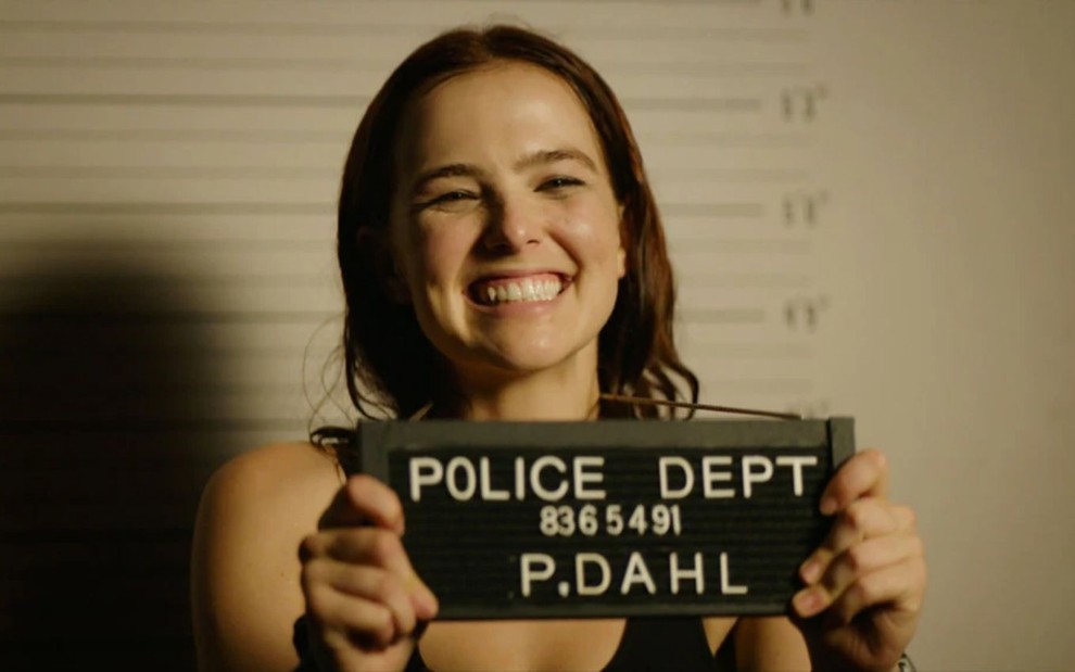 Zoey Deutch sorri com cartão de identificação da cadeia em cena do filme Como Sair de Buffalo