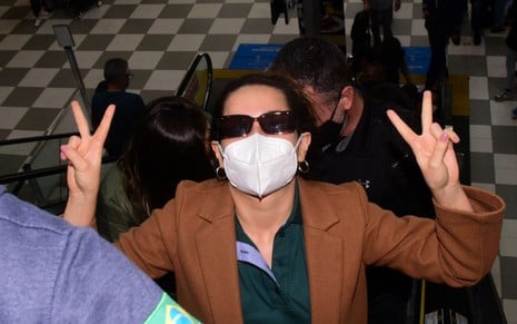 Juliette de máscara e óculos de sol em escada rolante do aeroporto de São Paulo