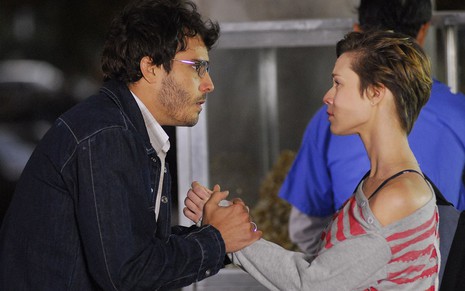 Os atores Thiago Rodrigues e Mariana Ximenes como Cassiano e Lara em A Favorita; eles estão de lado, se olhando frente a frente, enquanto ele segura as mãos dela