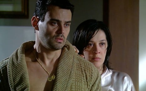 Os atores Carmo Dalla Vecchia e Claudia Raia como Zé Bob e Donatela em A Favorita; ele está de roupão, olhando para frente com cara de assustado, enquanto ela está atrás, segurando em seu ombro e também olhando com cara de assustada