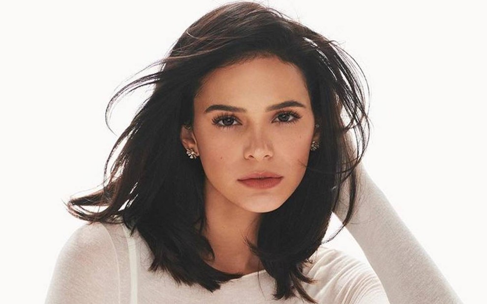 Bruna olha para a câmera, veste body branco e está com o cabelo solto