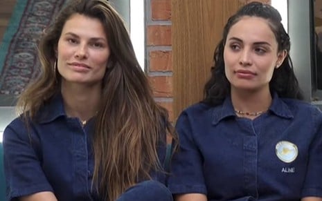 Dayane veste um macacão azul e está ao lado de Aline; Aline olha para o lado e veste macacão azul