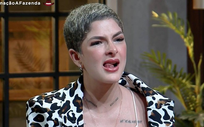 Lary olha para baixo, veste terno com estampa preta e branca e usa blusa branca